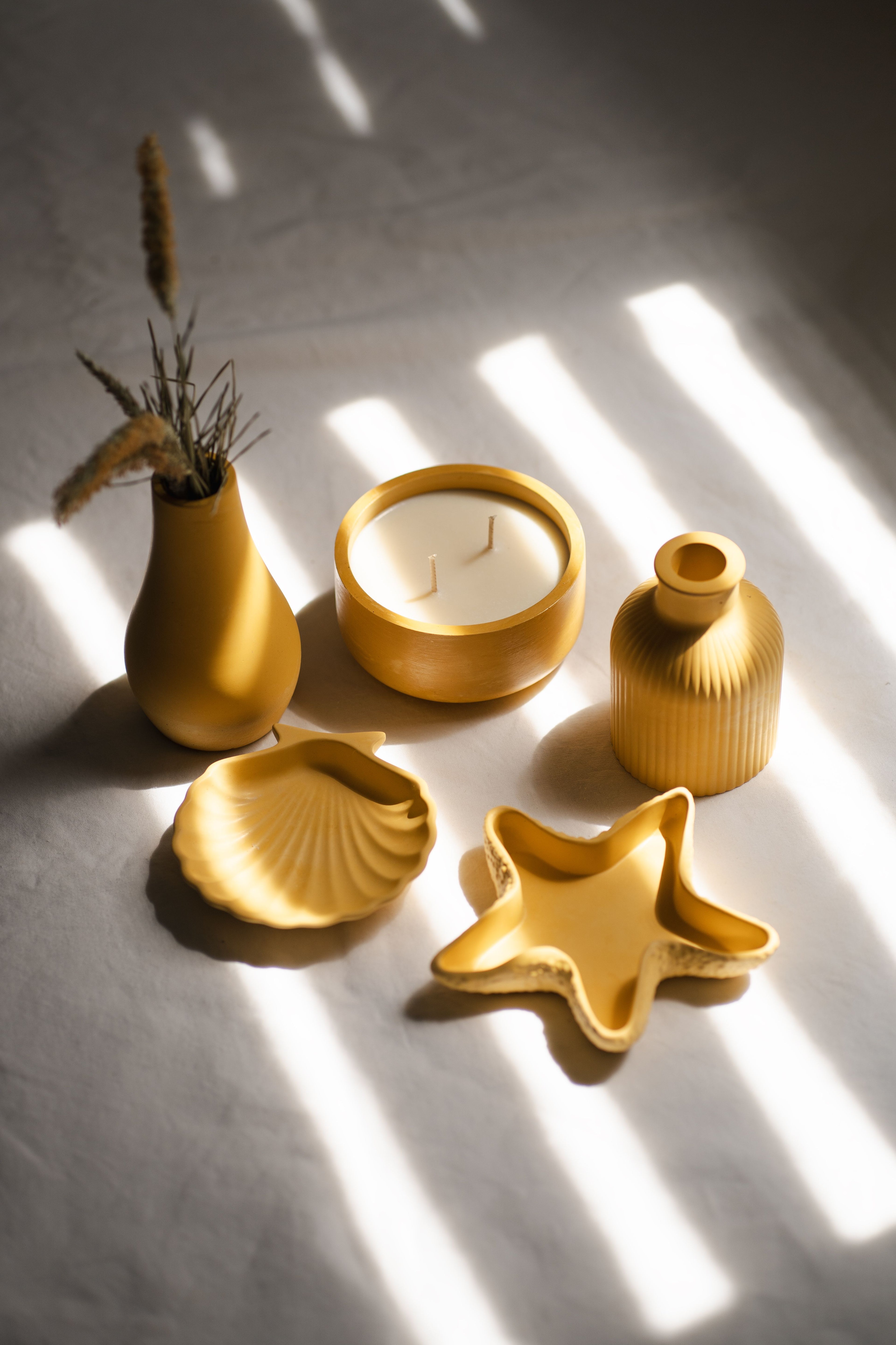 Set of yellow ceramic items including a shell, starfish, and decorative vases on a light surface with shadows.